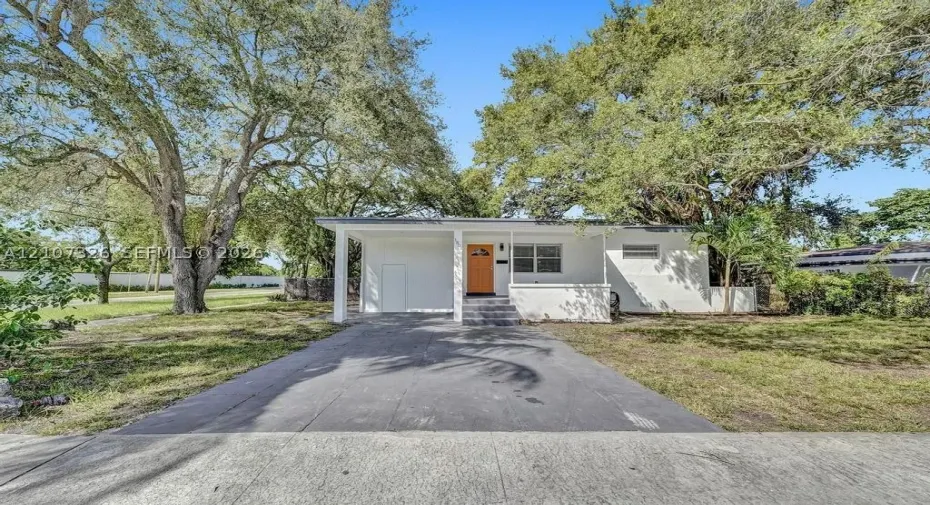 Single-story exterior featuring white stucco siding, a covered front entryway, concrete driveway, and mature landscaping