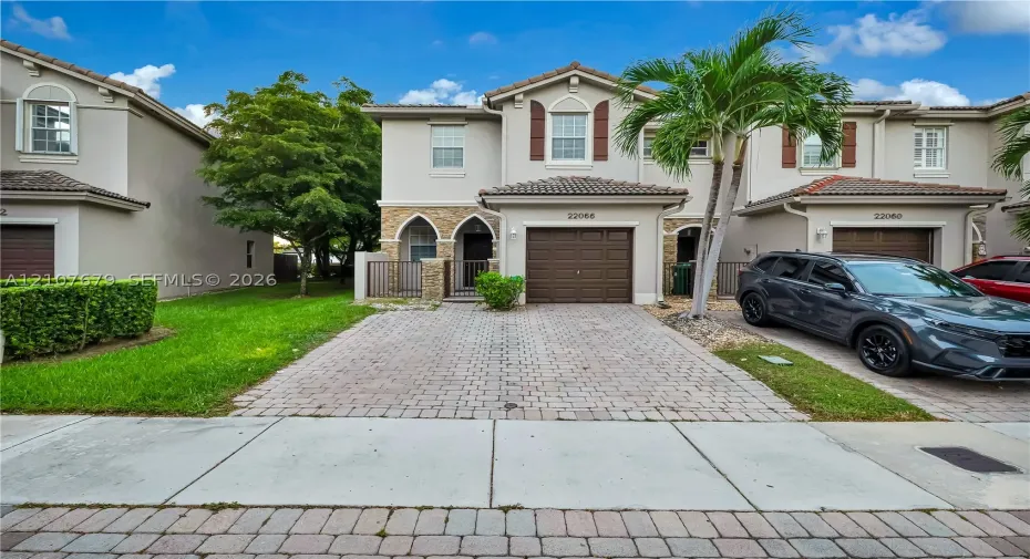 Two-story exterior featuring a paver driveway, stone facade accents, arched entryway, and clay tile roof