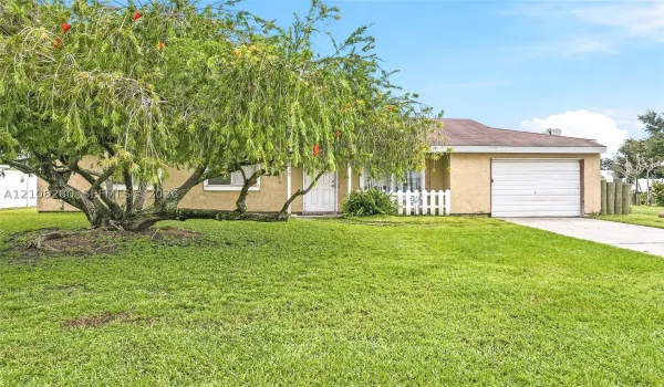 Stucco exterior featuring a concrete driveway, attached one-car garage, and picket fencing