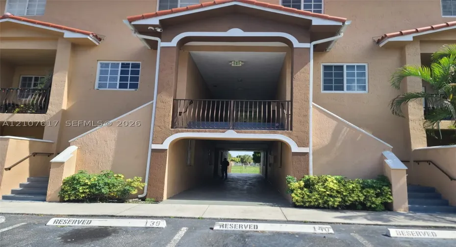Stucco exterior with an arched entryway, elevated balcony featuring metal railings, and two sets of concrete exterior stairs
