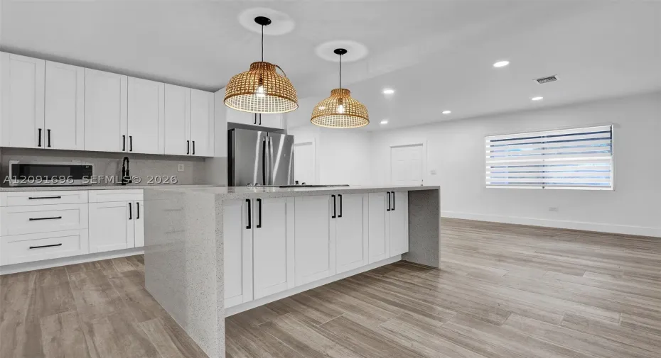 Kitchen featuring white Shaker-style cabinetry, a quartz-surfaced waterfall island, wood-finish flooring, recessed lighting, and woven pendant fixtures