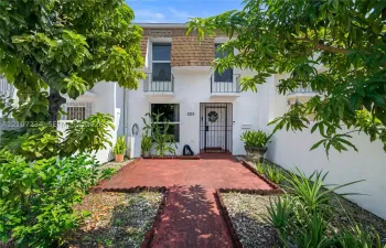 Exterior facade featuring white stucco finish, second-story decorative iron balcony railings, a metal security door, and a painted masonry walkway