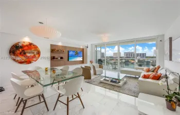 Open-concept living area featuring light-toned flooring with stone-pattern detail, built-in wood-finish shelving, recessed ceiling lighting, and floor-to-ceiling glass panels