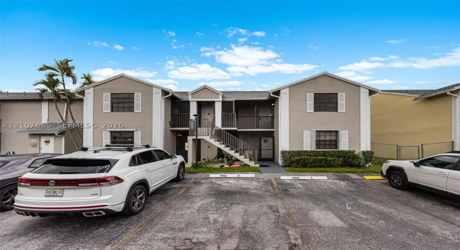 Two-story exterior featuring a neutral stucco facade, white trim accents, gabled rooflines, designated parking spaces, and covered entryways