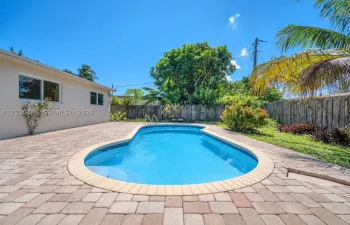 In-ground pool with stone coping, paver patio, wood-style privacy fencing, and established perimeter landscaping