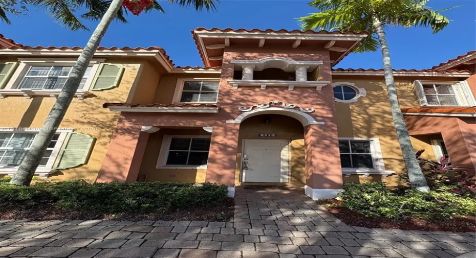 Mediterranean-style exterior featuring a clay tile roof, arched entryway, decorative stucco detailing, multi-pane windows with shutters, and a stone-paver walkway