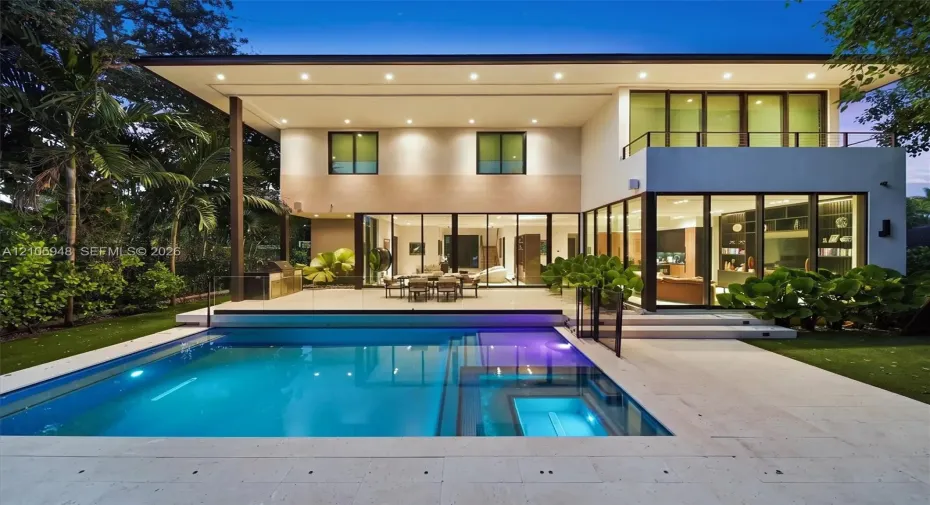Modern two-story exterior featuring floor-to-ceiling glass sliding doors, a flat roofline, an integrated swimming pool with a stone patio surround, and a second-story balcony with a metal railing