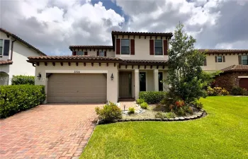Two-story exterior featuring a stucco façade, decorative corbel roof supports, a multi-textured clay tile roof, and a paved brick driveway and walkway