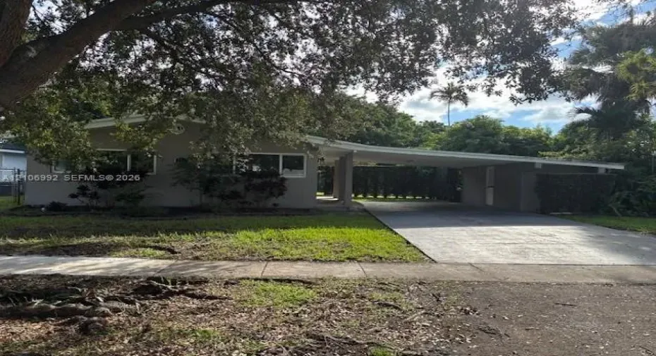 Single-story exterior featuring a low-pitch roofline, integrated carport, concrete driveway, and front lawn with mature canopy trees