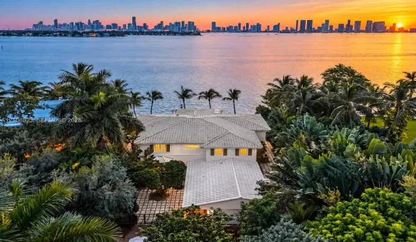 Waterfront estate featuring a tile roof, paved courtyard, lush landscaping, and a direct city skyline backdrop