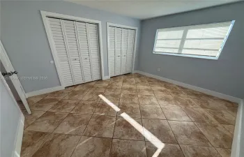 Tile flooring arranged in a diagonal pattern, two sets of white louvered-style closet doors, and a horizontal sliding window