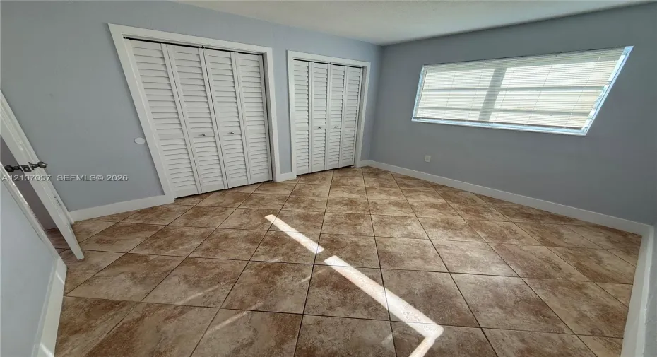 Tile flooring arranged in a diagonal pattern, two sets of white louvered-style closet doors, and a horizontal sliding window