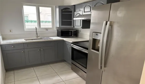Kitchen featuring gray shaker-style cabinetry, white solid-surface countertops, stainless steel appliances, and tile flooring