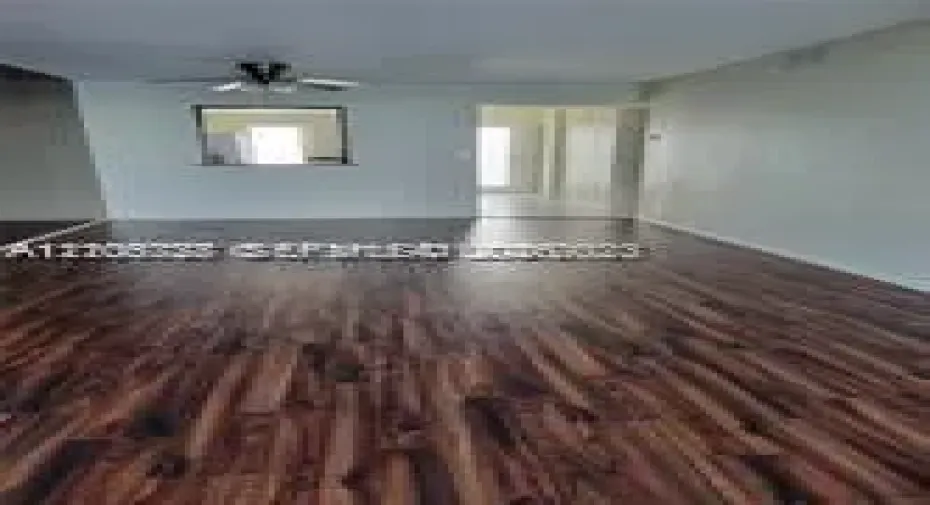 Open floor plan featuring wood-finish flooring, a ceiling fan with integrated lighting, and a pass-through wall opening