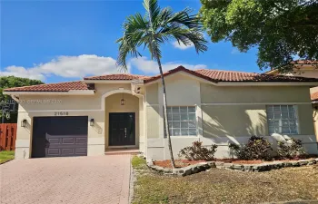 Stucco exterior featuring a red tile roof, arched entryway, paved driveway, and grid-patterned windows