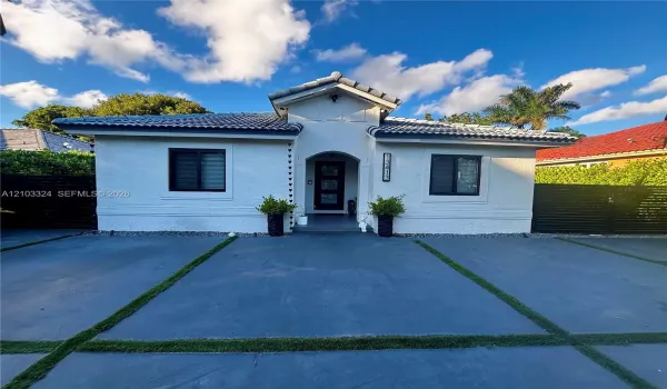 Stucco exterior with a tiled roof, arched entryway, and a concrete driveway featuring inlaid grass borders