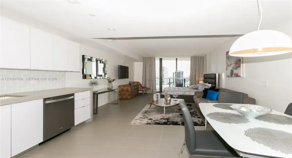 Contemporary kitchen featuring white flat-panel cabinetry, a light-toned tile backsplash, and a metallic-finish dishwasher, complemented by large-format floor tiling and floor-to-ceiling glass patio doors