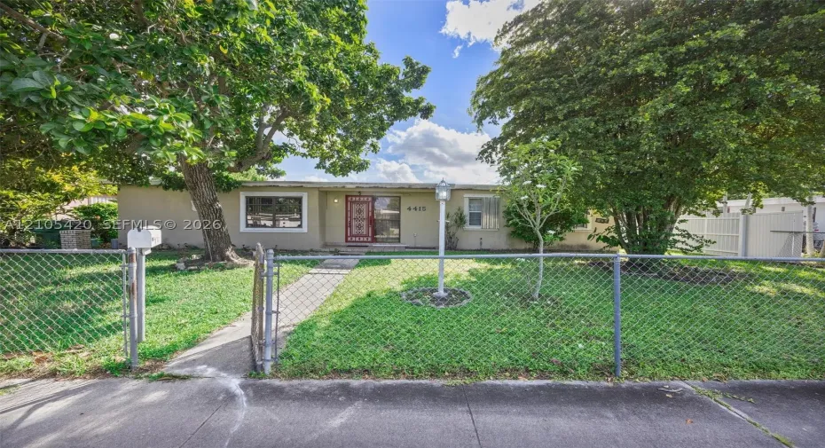 Single-story residence featuring a chain-link fence, concrete pathway, and mature trees