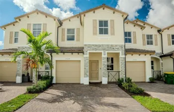Stucco exterior featuring stacked stone accents, decorative shutters, a paved driveway, and tile roofing