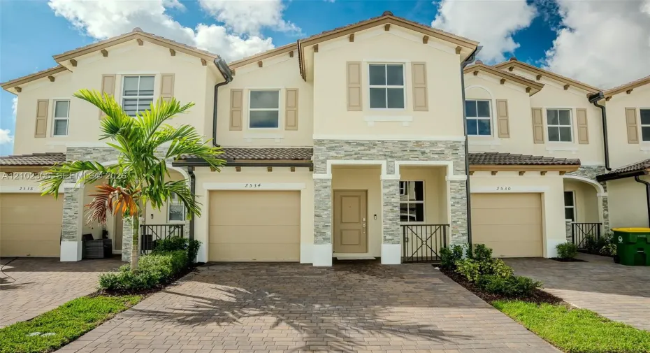 Stucco exterior featuring stacked stone accents, decorative shutters, a paved driveway, and tile roofing