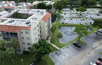 Multi-story residential building featuring a terracotta tile roof, balcony enclosures, landscaped grounds, a central fountain, and dedicated parking areas