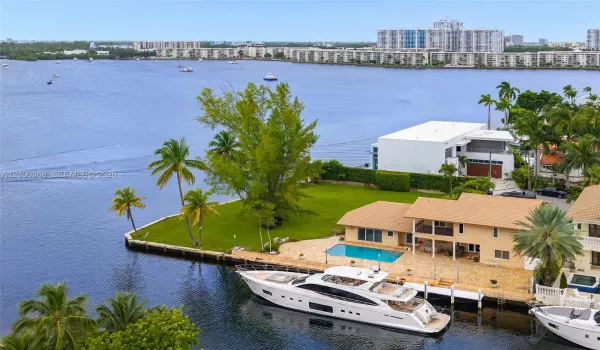 Waterfront property featuring a private boat dock, swimming pool, concrete seawall, expansive lawn, and mature palm trees