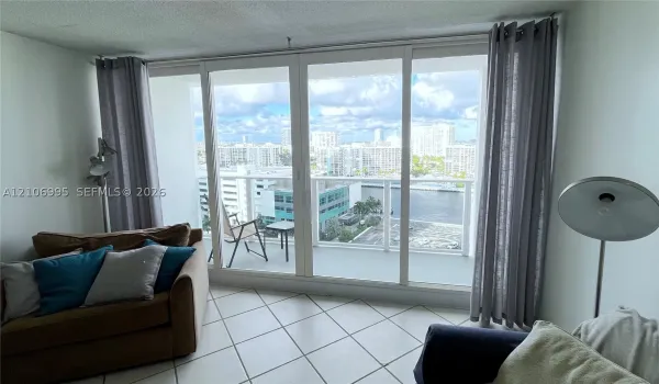 Floor-to-ceiling glass sliding doors, private balcony with glass railing, ceramic tile flooring, and urban water scenery