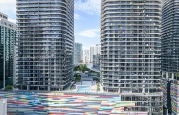 High-rise residential towers featuring wrap-around glass balconies, exterior multi-colored mural facade, and outdoor swimming pool