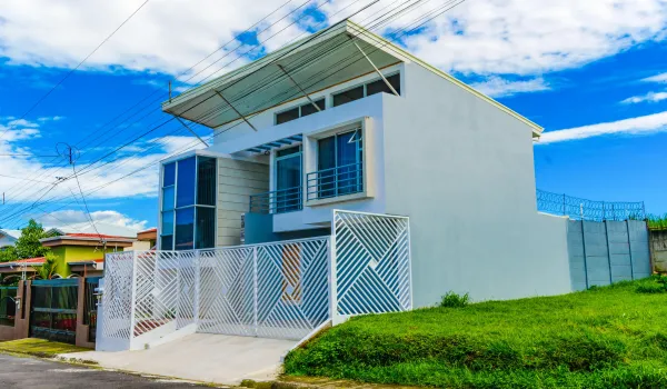 Contemporary two-story exterior featuring a shed-style roof, floor-to-ceiling multi-pane windows, balcony with metal railing, and a geometric white privacy gate