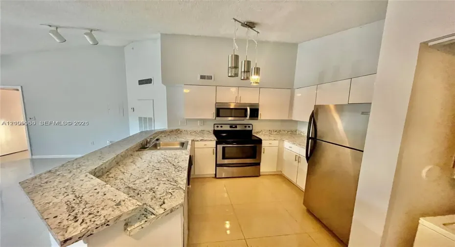 Kitchen featuring a raised breakfast bar with stone-finish countertops, white cabinetry, stainless steel appliances, and multi-light pendant illumination