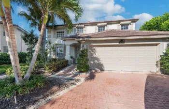Two-story exterior featuring a stucco facade, tiled roof, paved driveway, and mature landscaping