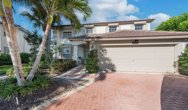 Two-story exterior featuring a stucco facade, tiled roof, paved driveway, and mature landscaping