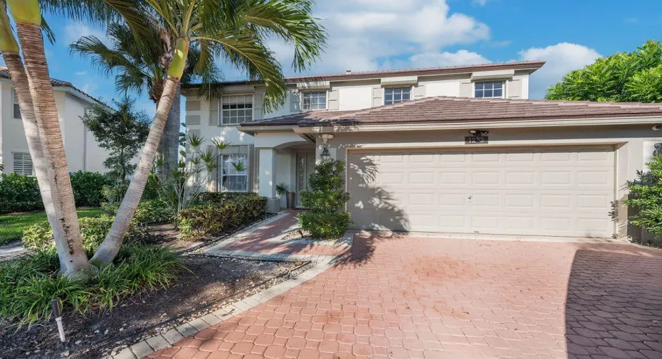 Two-story exterior featuring a stucco facade, tiled roof, paved driveway, and mature landscaping