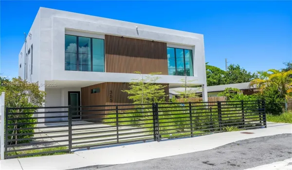 Contemporary two-story exterior featuring smooth stucco siding, wood-finish paneling, large-format glass windows, and a metal horizontal-slat security gate
