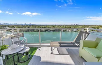 Private balcony featuring tile flooring, artificial turf accents, and a glass-paneled railing with open water and skyline scenery