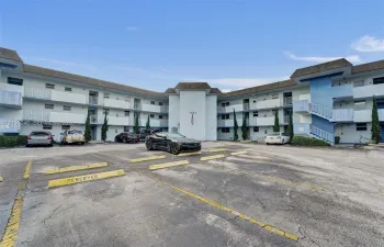 Multi-story apartment building exterior featuring paved surface parking, covered exterior corridors, and vertical landscaping accents
