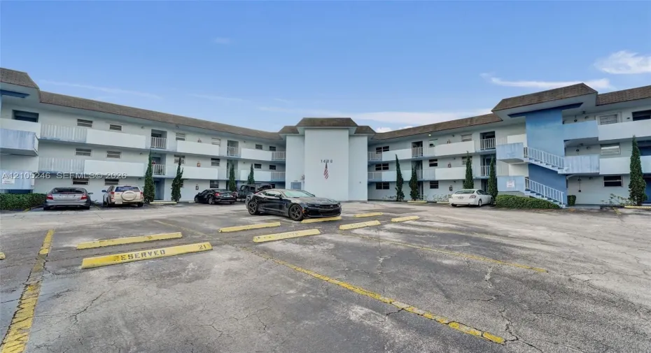 Multi-story apartment building exterior featuring paved surface parking, covered exterior corridors, and vertical landscaping accents