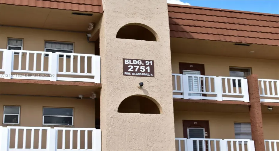 Multi-story stucco exterior featuring arched architectural accents, clay-tile roofing, and white picket-style balcony railings