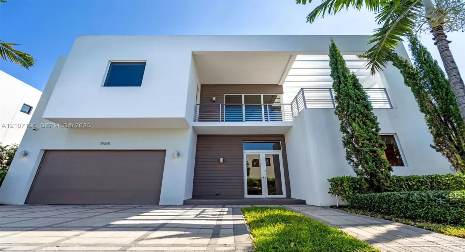 Modern two-story architectural exterior featuring smooth white stucco finish, horizontal wood-panel siding, upper-level balcony with metal railing, and paver driveway