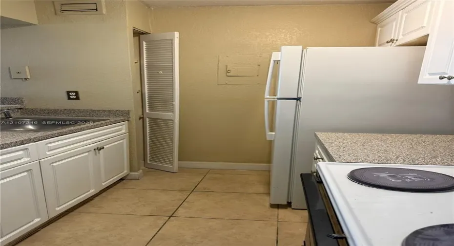 Kitchen featuring white cabinetry, stone-finish countertops, stainless steel sink, tile flooring, and a louvered-door pantry