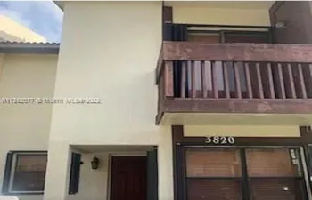 Stucco exterior featuring a wood-rail balcony, dark-frame windows, and a recessed entrance