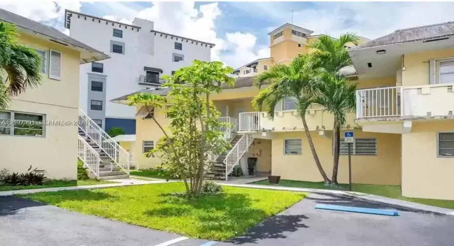 Multi-level exterior featuring light-toned stucco siding, open-air metal staircases, elevated private balconies with metal railings, and a landscaped courtyard