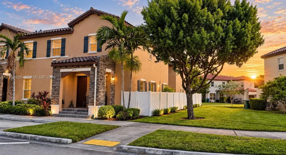 Two-story exterior featuring a stucco façade, stacked stone entry detailing, decorative exterior shutters, and an attached white vinyl privacy fence