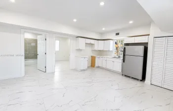Kitchen area featuring white shaker-style cabinetry, stainless steel refrigerator, stone-patterned tile flooring, recessed ceiling lighting, and louvered closet doors