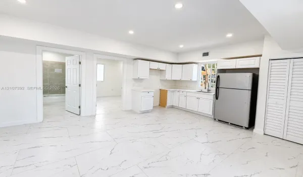 Kitchen area featuring white shaker-style cabinetry, stainless steel refrigerator, stone-patterned tile flooring, recessed ceiling lighting, and louvered closet doors