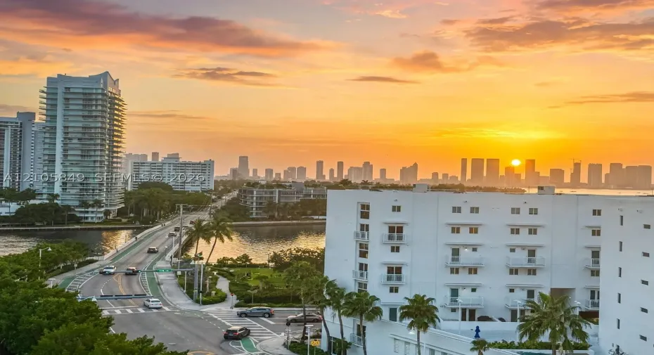 Aerial perspective featuring a multi-story white stucco exterior with recessed balconies and a skyline backdrop