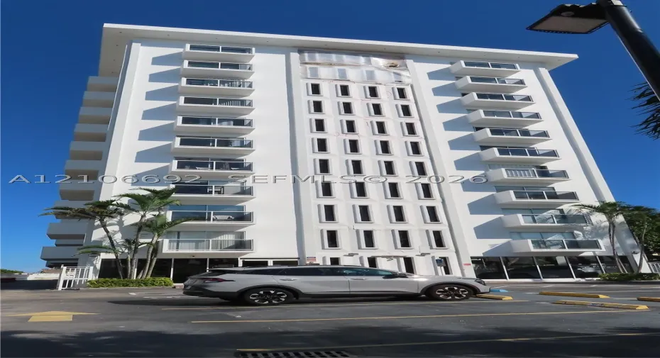 Multi-story high-rise exterior featuring a white facade, repeating glass-panel balconies, and vertical architectural detailing