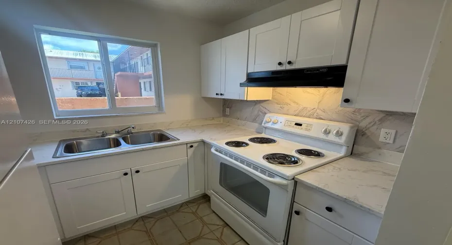 Kitchen featuring white shaker-style cabinetry, patterned stone-finish countertops, herringbone-patterned tile backsplash, stainless steel dual-basin sink, and a white electric range