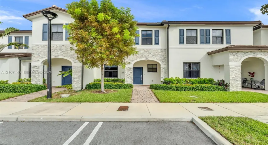 Multi-unit exterior featuring a light-colored stucco finish, decorative stone veneer accents, arched entryways, and brick-paver walkways