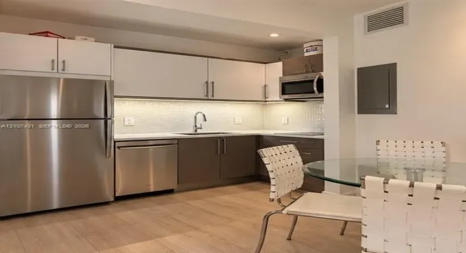 Kitchen featuring stainless steel appliances, two-tone cabinetry, quartz countertops, a textured tile backsplash, and wood-finish flooring